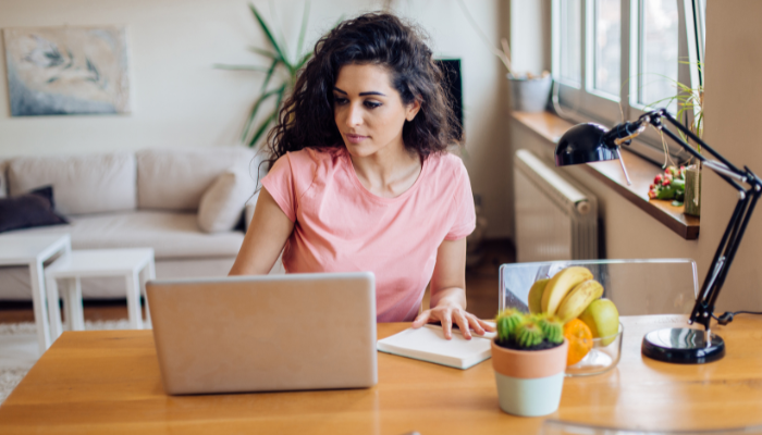 Woman applying to housing online with laptop at table with fruit and cactus nearby.