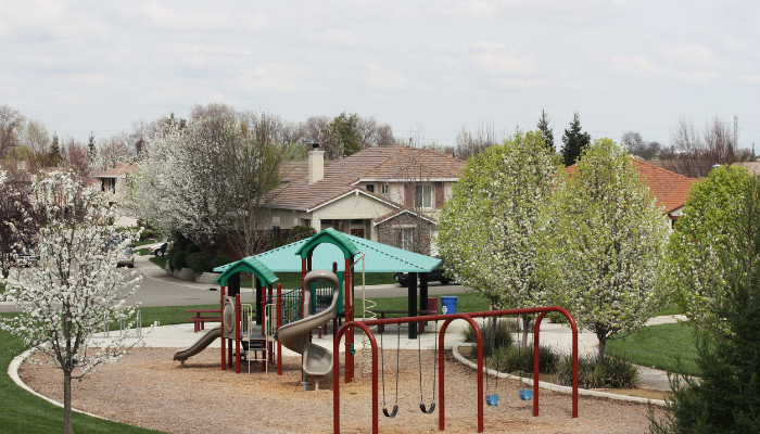 Neighborhood playground in military housingwith green roof and swings with blooming trees and houses around. 