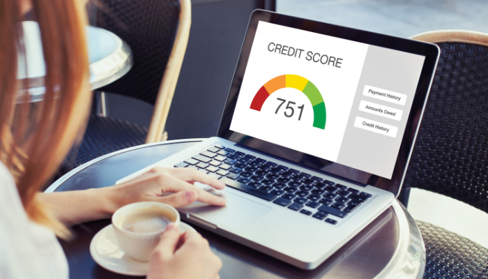 Woman sits with coffee mug while checking her credit score on laptop computer.