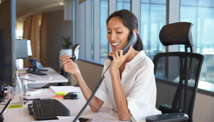 Woman in white button down smiles in office while on phone. 