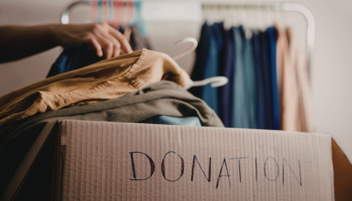Person laying clothes over cardboard box marked "Donation"