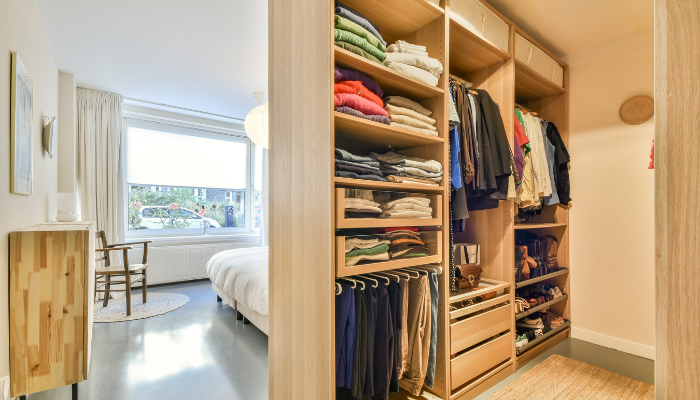 Large organized closet with folded and hanging clothing with entrance to bedroom in view.