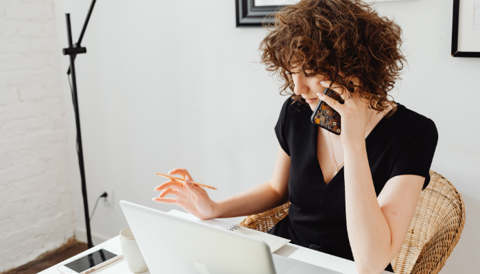 Woman talking on cell phone at desk in front of computer. 