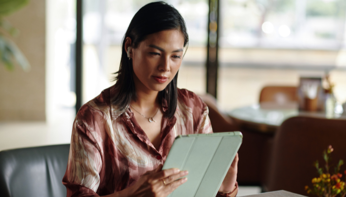 Woman in red pattern shirt reads on iPad with green case.