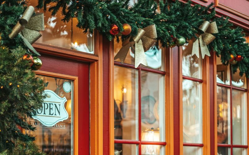 storefront with glass windows and red door decorated with holiday themed garland, ribbons, and ornmaents Holiday_Events_in_Alexandria,_VA