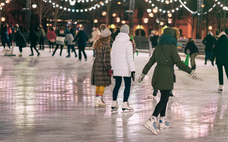 Girls ice skating at festive holiday outdoor ice rink.