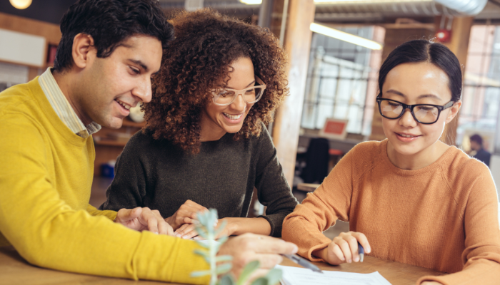 Man in yellow shirt and woman in glasses meet with woman to look over rental paperwork on table.