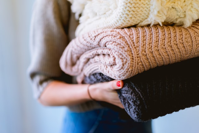woman holding stack of clean sweaters