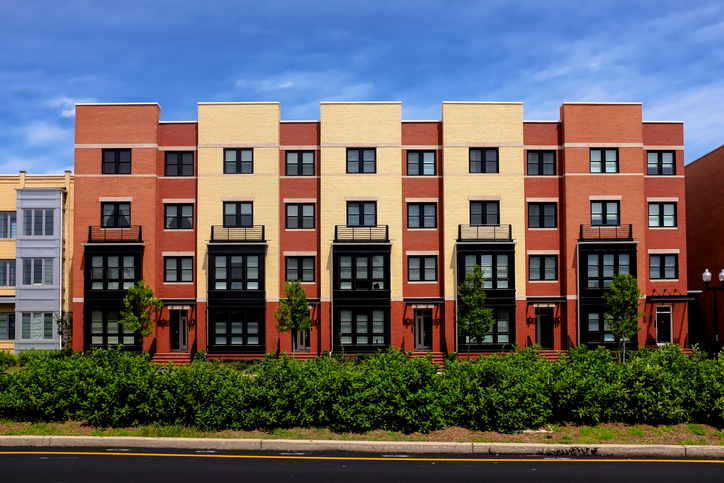 row of dark orange and tan apartment buildings with green bushes and blue sky in Alexandria VA